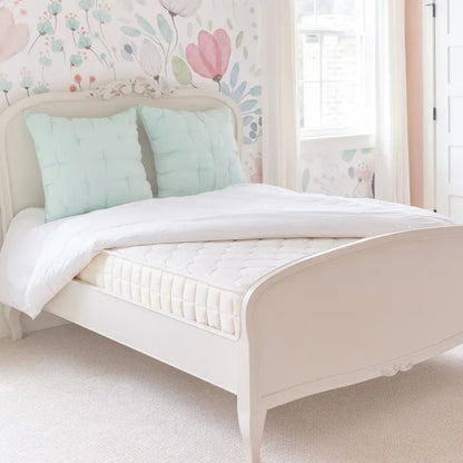 White bed with light blue pillows in a child's bedroom with floral wallpaper.