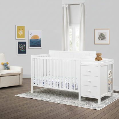 White wooden baby crib with a matching three-drawer dresser and side changing table, styled in a bright nursery with framed wall art, a window, and a small teddy bear on the dresser.