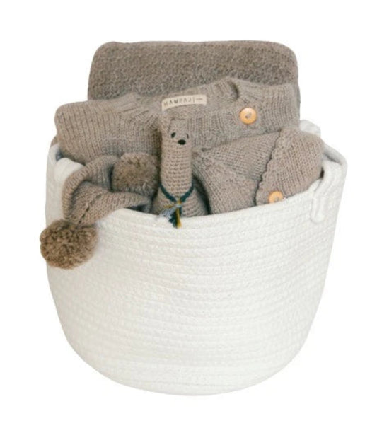A collection of soft baby accessories, including a gray knit blanket, cardigan, and plush toy, arranged inside a white woven basket on a white background.