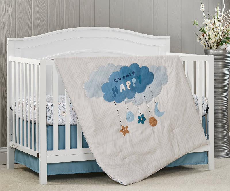 White crib with a decorative cloud-themed blanket featuring the word 'HAPPY' on a wooden floor.