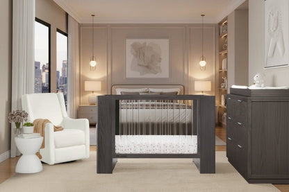 Modern nursery with dark wood crib, white chair, and large window view.