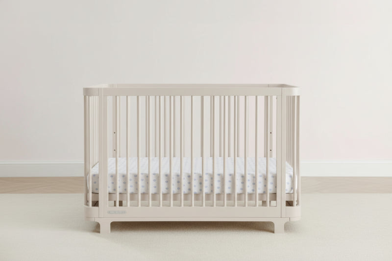 Beige crib with white mattress on a light gray background