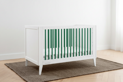 White crib in a room with green paneled walls and a wooden floor.