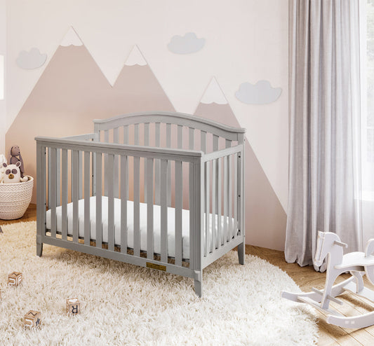Gray crib in a nursery with mountain wall decor and a rocking horse.