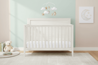 White crib in a nursery with a teddy bear and decorative items on a light green wall.