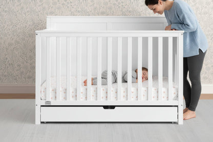 White crib with a mattress and drawers on a neutral background