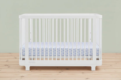 White crib with a blue and white crib sheet on a white background