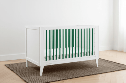 White crib in a room with green paneled walls and a wooden floor.