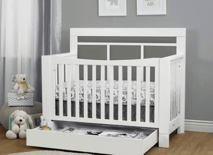 White crib with a gray mattress in a room with gray walls and white curtains.